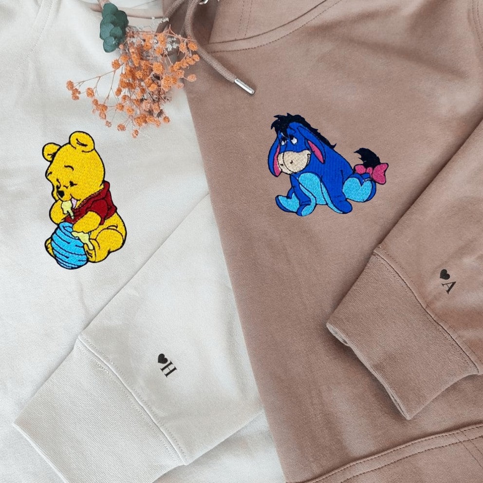 "Close-up of embroidered Winnie the Pooh and Eeyore designs on unisex hoodies."