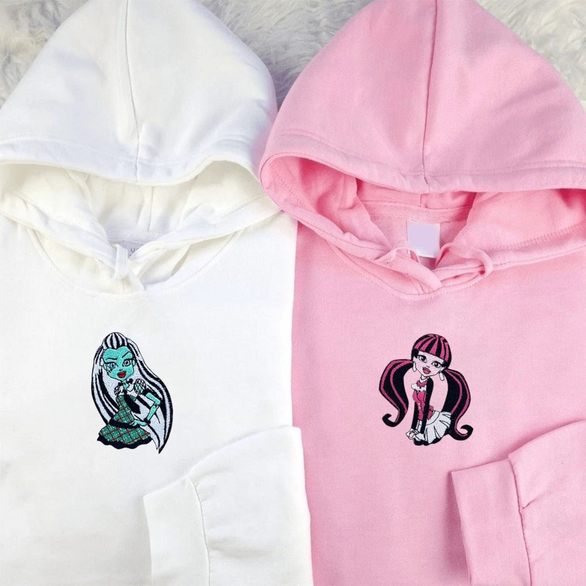 Soft pink and blue hoodies with playful embroidered monster character designs.