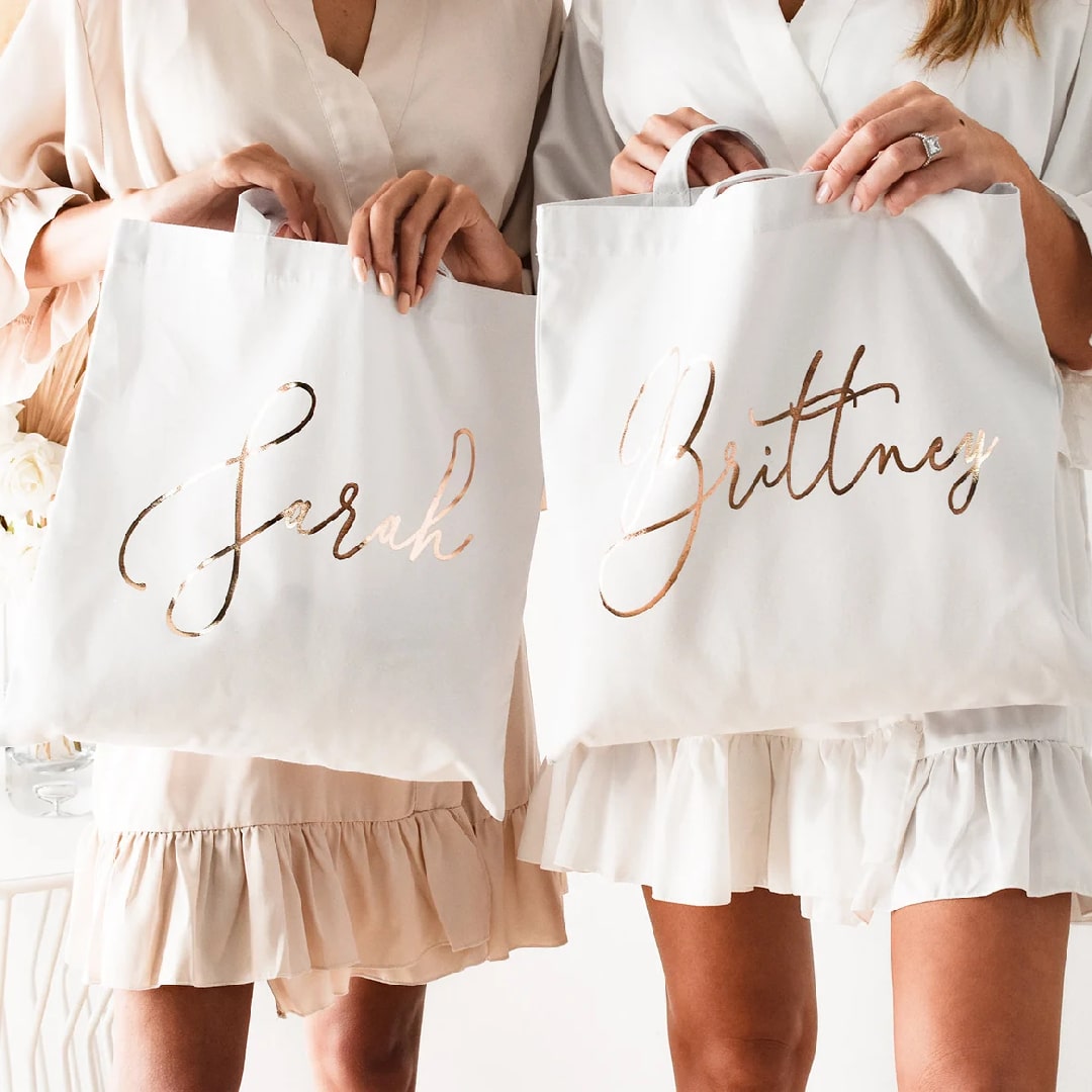 Personalized bridesmaid tote bags with metallic script lettering for wedding gifts.