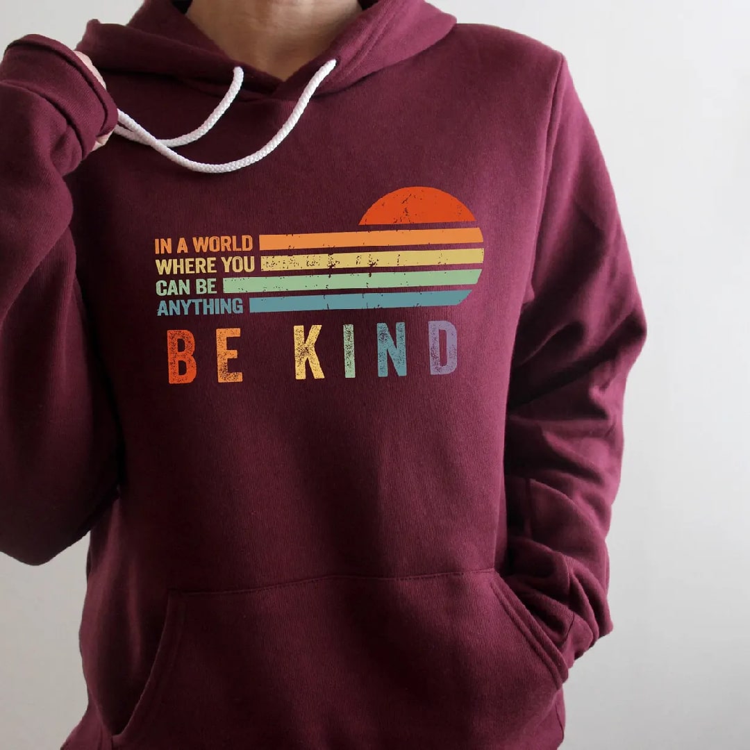 Maroon "Be Kind" sweatshirt with vibrant rainbow sunset illustration