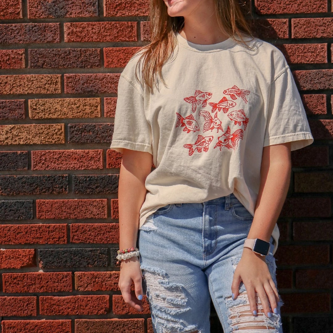 Casual outfit with fish print graphic t-shirt, denim skirt, and sneakers.