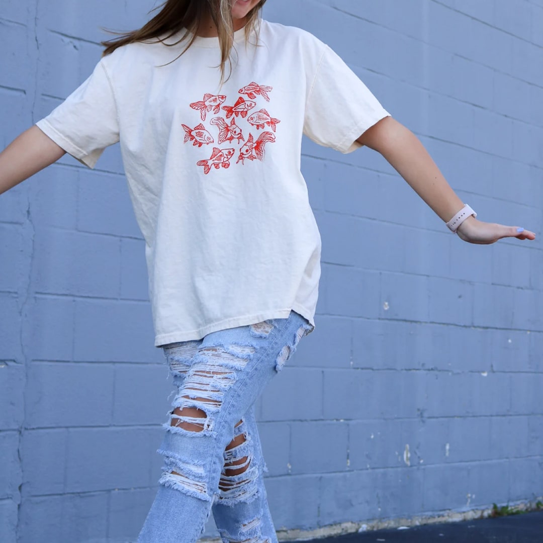 Model wearing fish print graphic t-shirt paired with distressed jeans.
