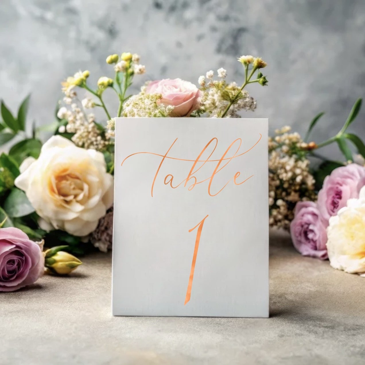 Gold foil wedding table number with floral decor in the background
