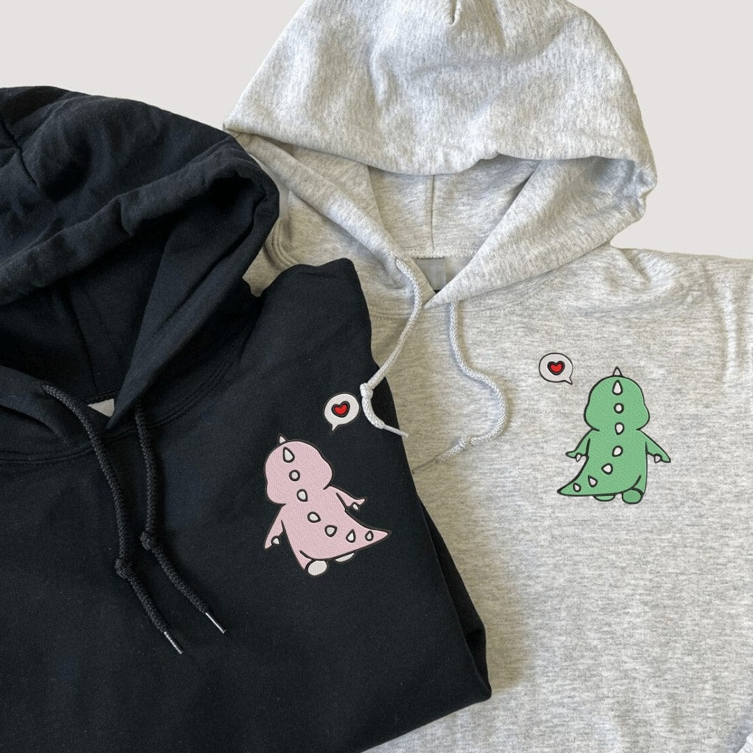 Matching pink and green dinosaur sweatshirts with heart embroidery.
