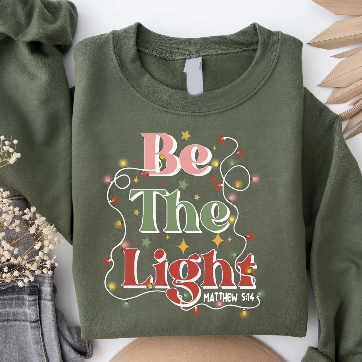 Festive Be The Light sweatshirt with Christmas decor elements for holiday style.