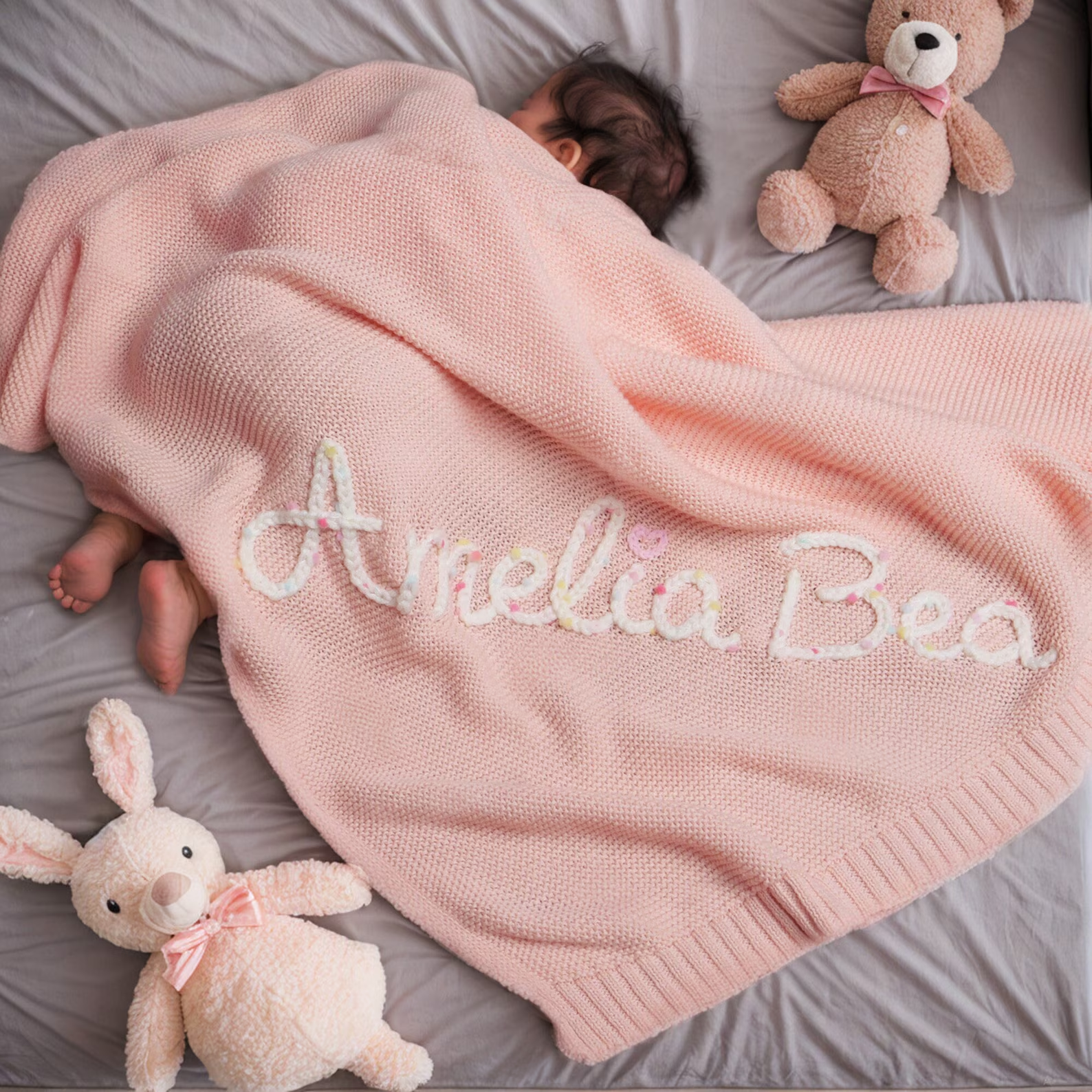 Pink personalized children's blanket with embroidered name in soft colorful letters.