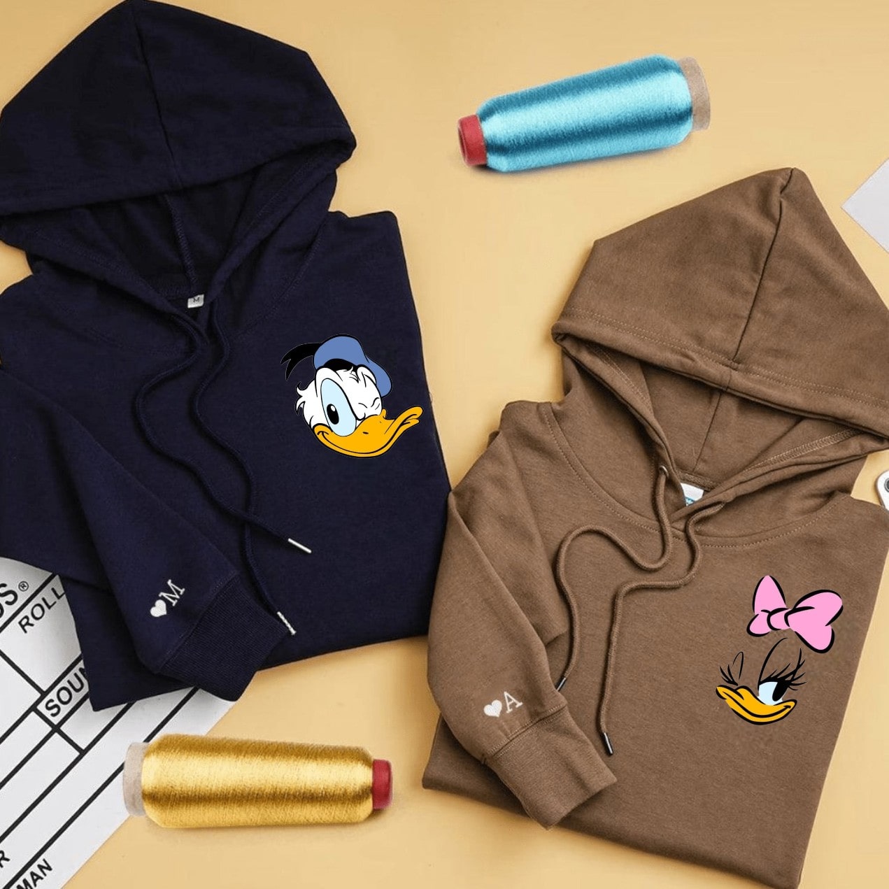 Matching couple hoodies featuring winking and bow-wearing duck designs.