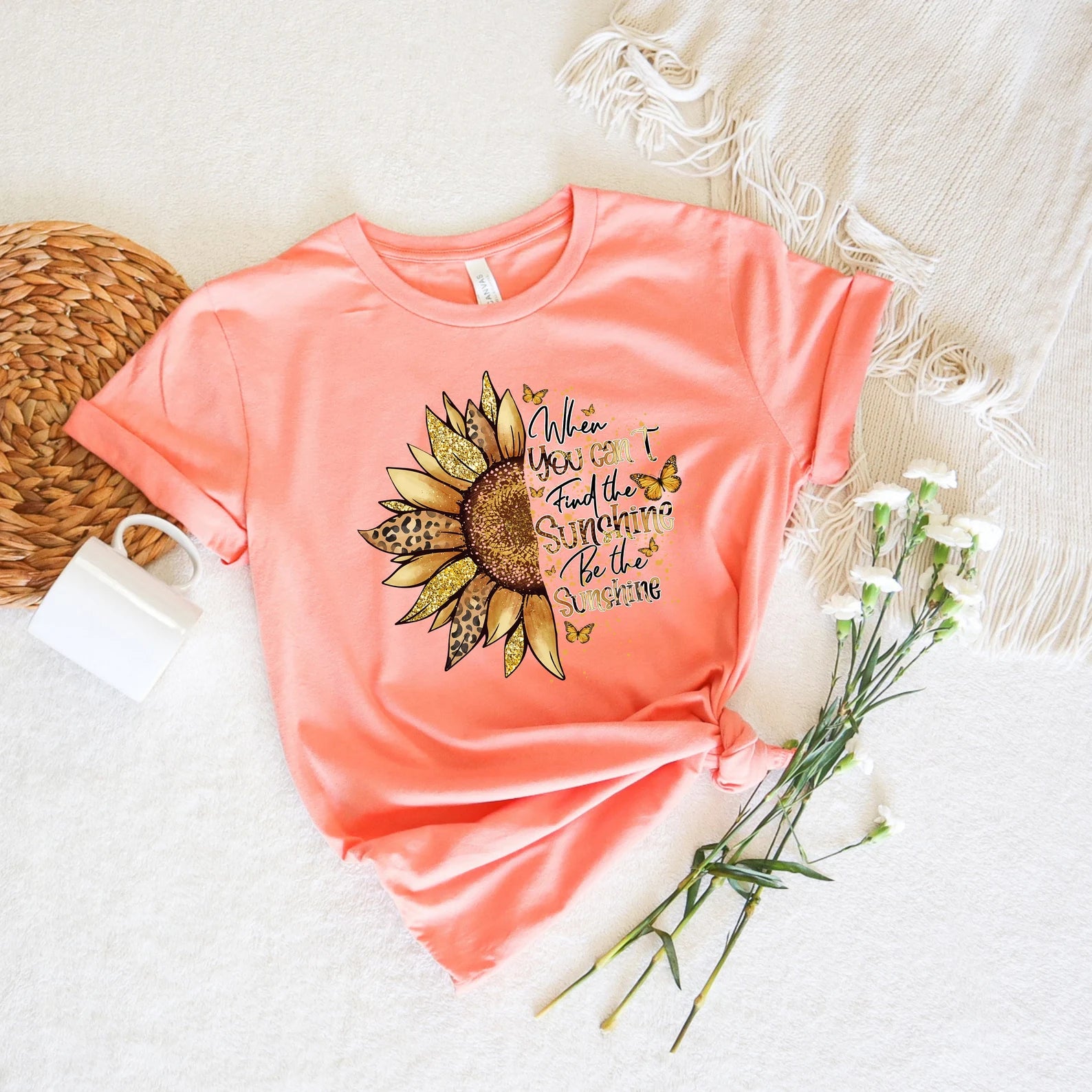 Close-up of sunflower graphic t-shirt in coral with golden, glittery accents and the text 'Be the sunshine‘