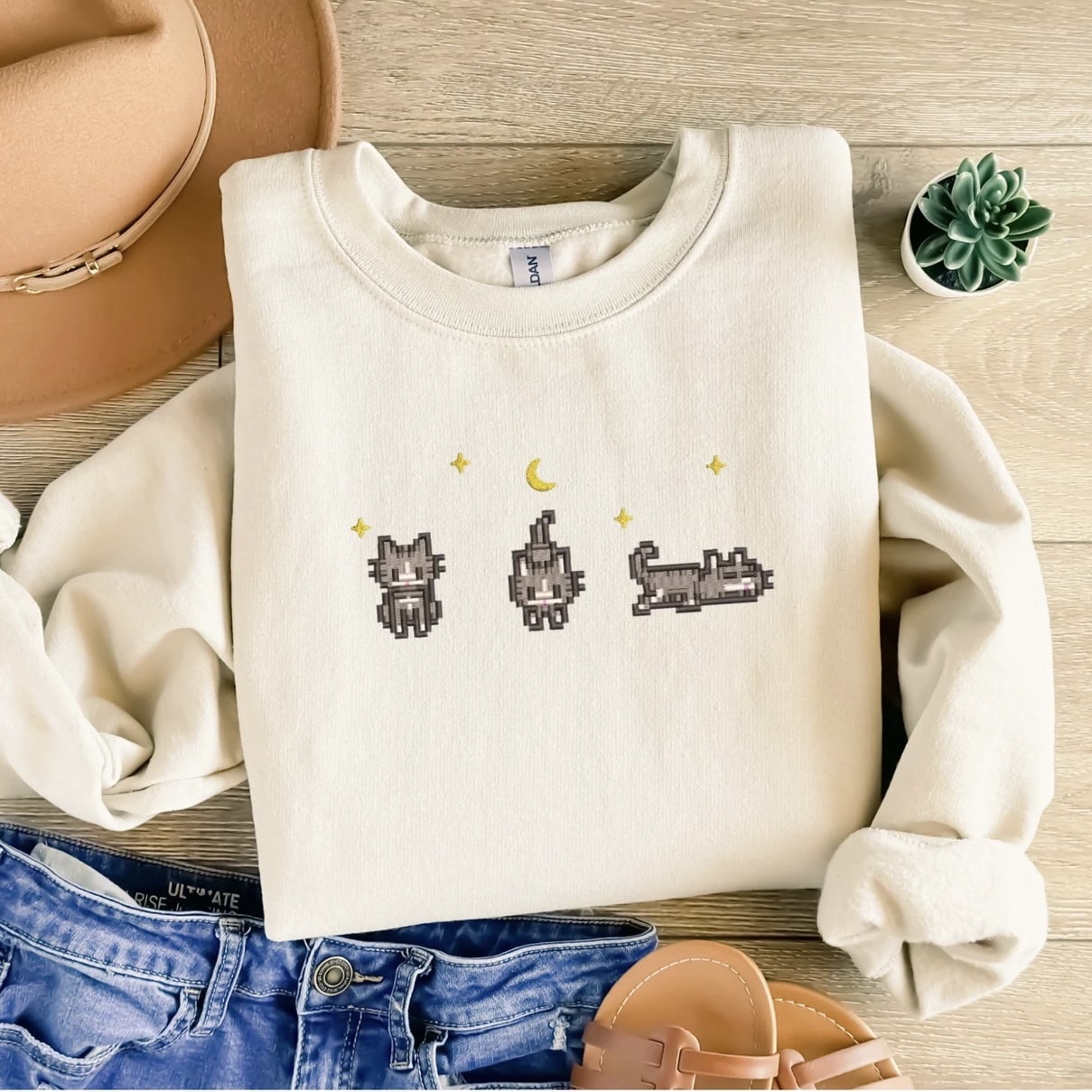 Stardew Valley-inspired beige sweatshirt with pixel art cats under moon and stars.