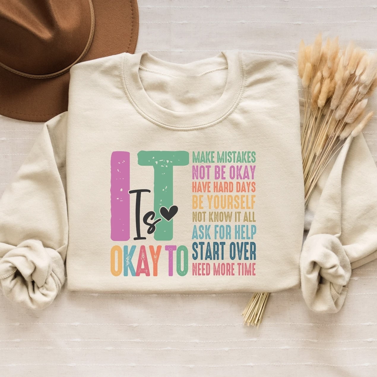 Beige crewneck sweatshirt featuring an uplifting message in pastel colors.