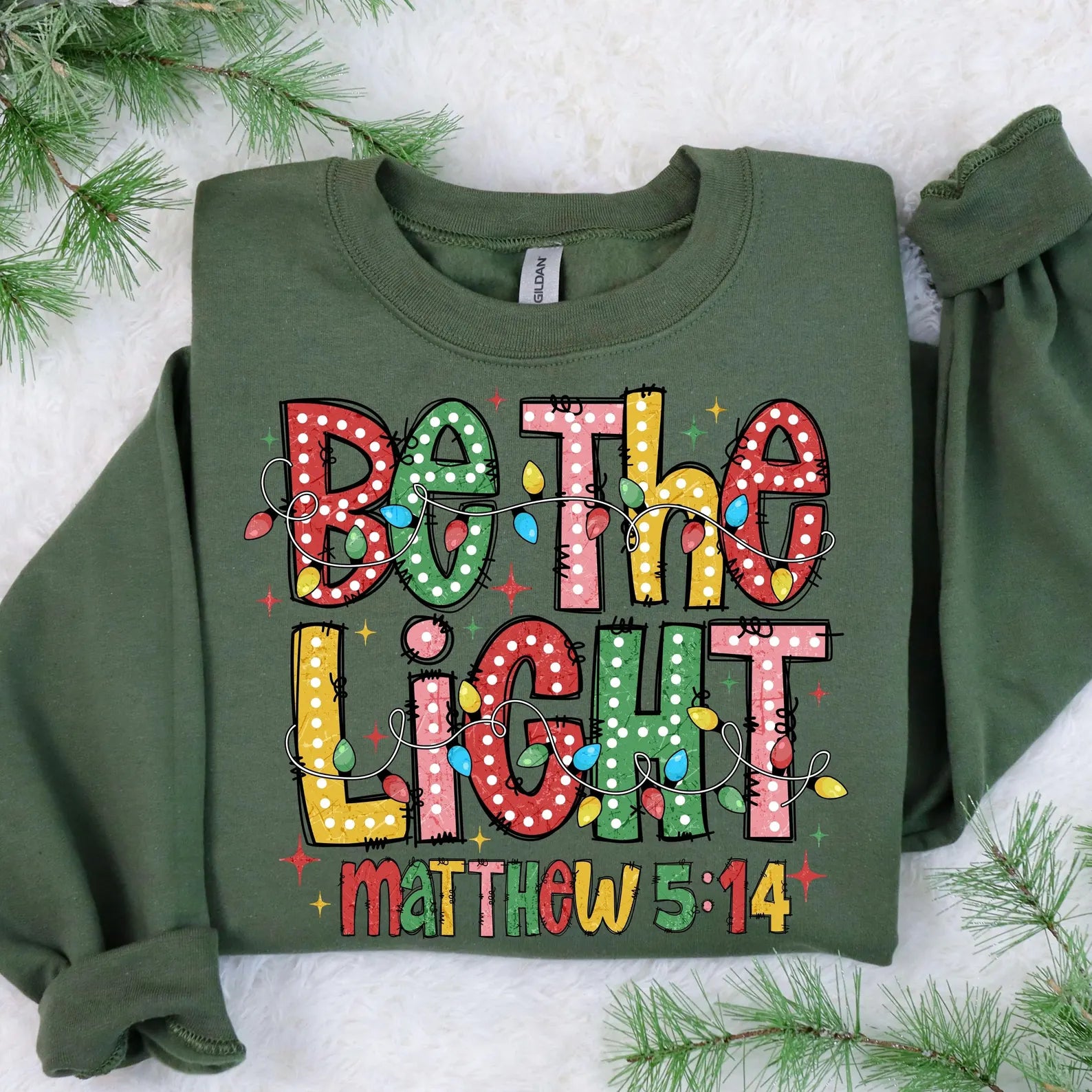 Soft and cozy Christian holiday sweatshirt with bold, colorful 'Be The Light' design.