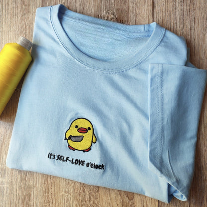 Custom embroidered graphic meme shirts featuring a yellow duck with "Self-LOVE o'clock" text, ideal for best gag gifts for men.
