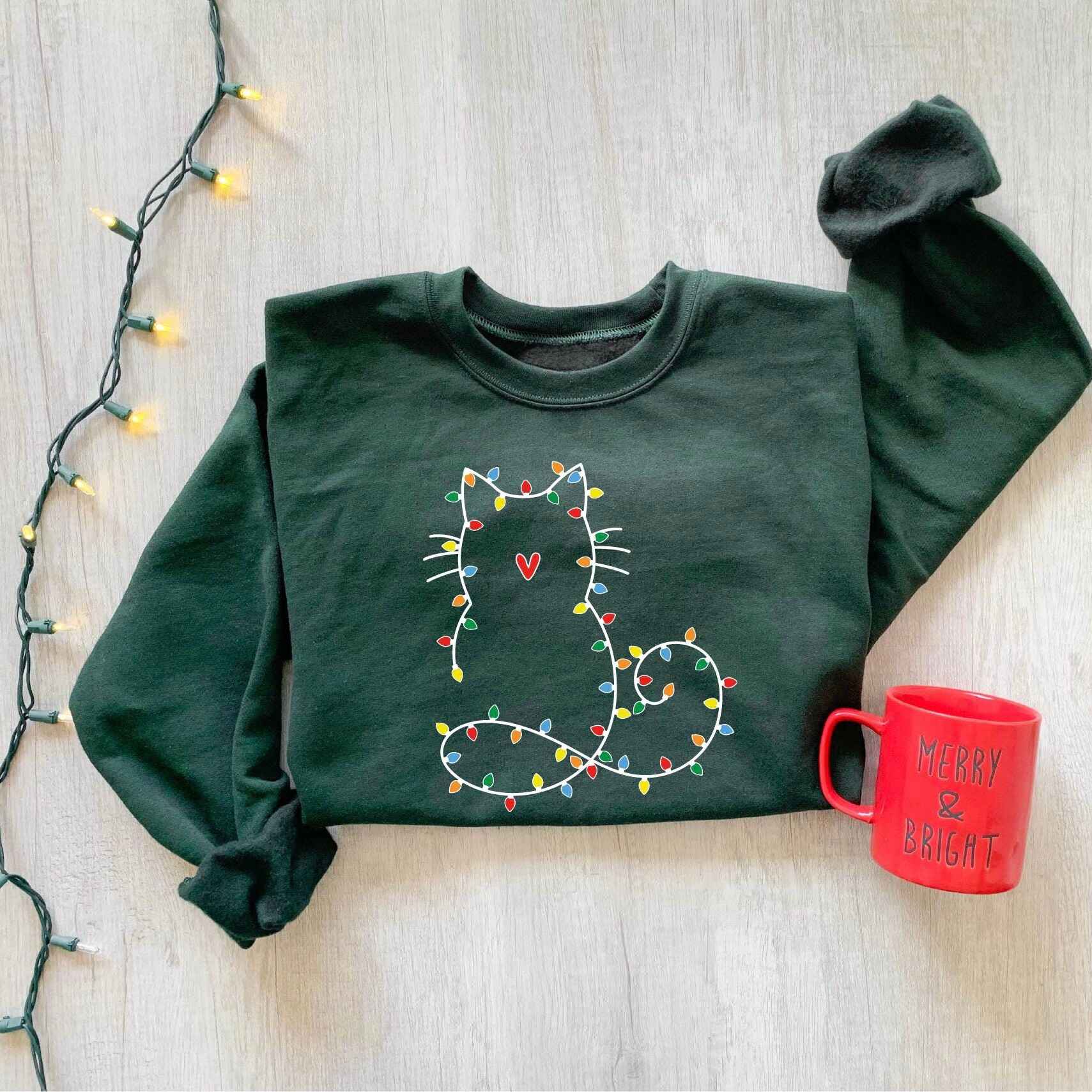 Cozy Christmas cat sweatshirt in pink with holiday light outline
